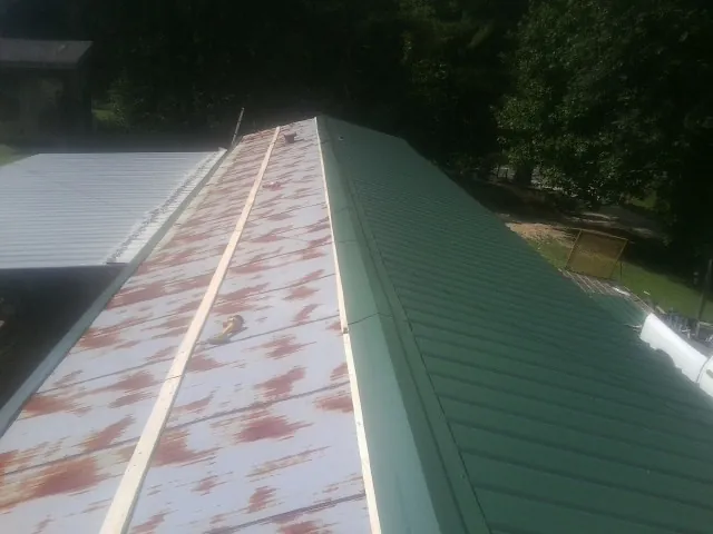 Old rusted panels beside newly installed green metal roofing — Wind Damage Roof Repair by Roofing Brothers in Allardt