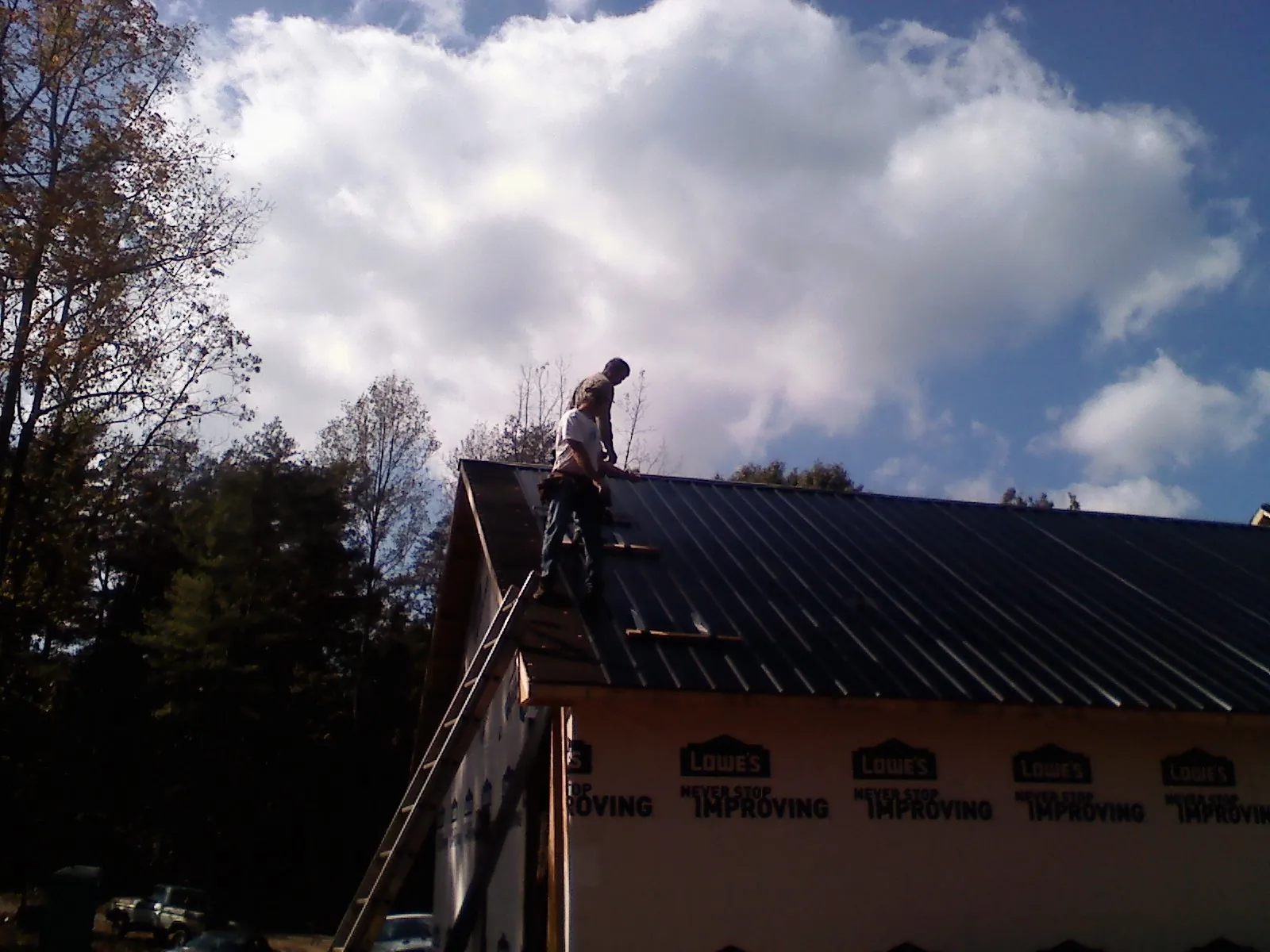 Roofer fastening dark metal panels high against a cloudy sky, from a Roof Inspection job in Allardt
