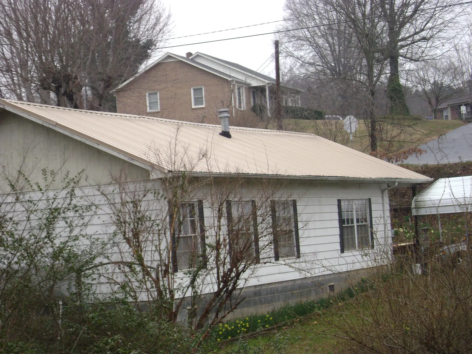 Tan metal roof on a white sided house set into a hillside — Commercial Roofing by Roofing Brothers in Allardt
