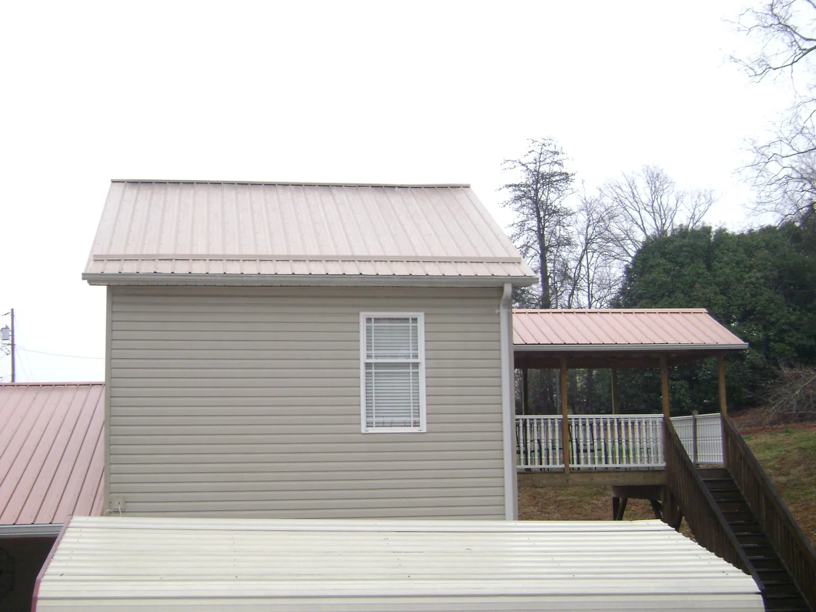 Tan metal roofs on a two story addition and attached porch, from a Roof Replacement job in Allardt